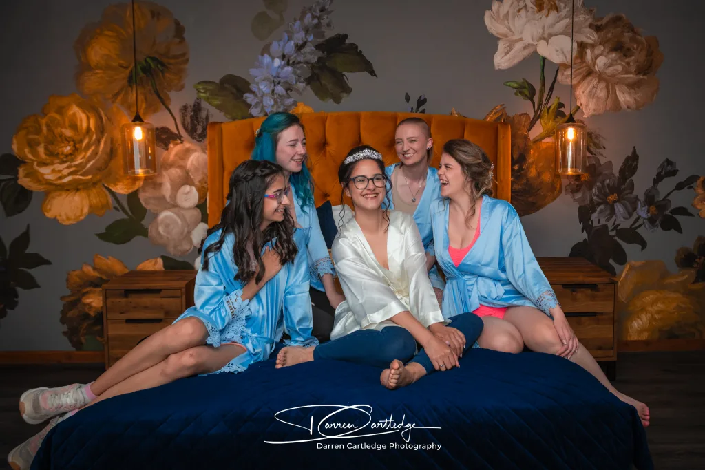 Bride sitting on bed surrounded by bridesmaids during morning preparations at a Yorkshire wedding