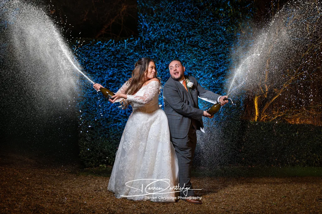 Johnathan and Leeann spraying champagne in the gardens at Bawtry Hall, celebrating with laughter and joy