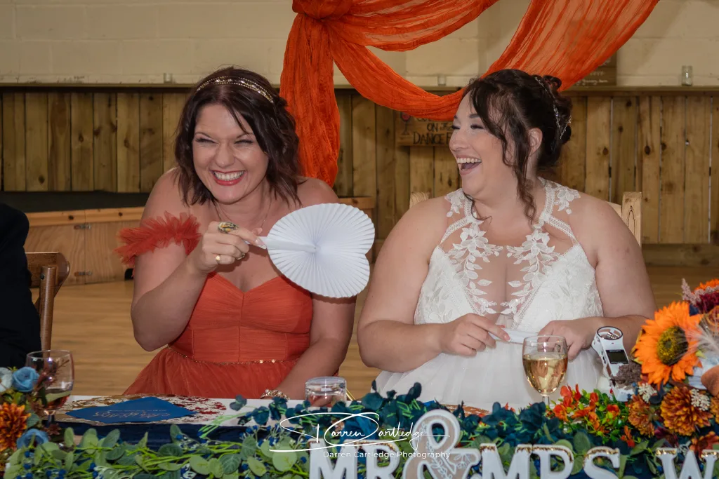 Bride and maid of honour laughing during speeches at Clapham Holme Farm barn wedding in Yorkshire