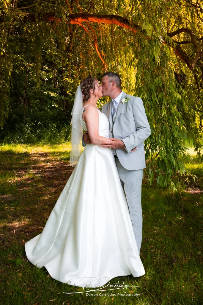 Bride and groom kissing under a weeping willow during a Yorkshire wedding