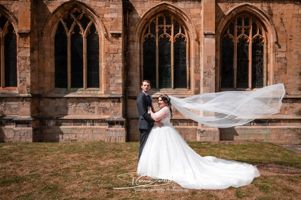 Bride and groom standing outside a church with the bride’s veil flowing during an East Yorkshire wedding