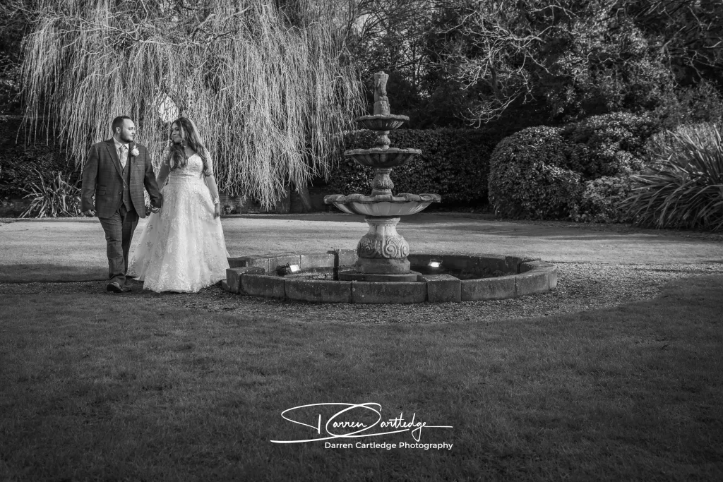 Leeann and Johnathan walking hand in hand by the fountain in the gardens at Bawtry Hall in Yorkshire
