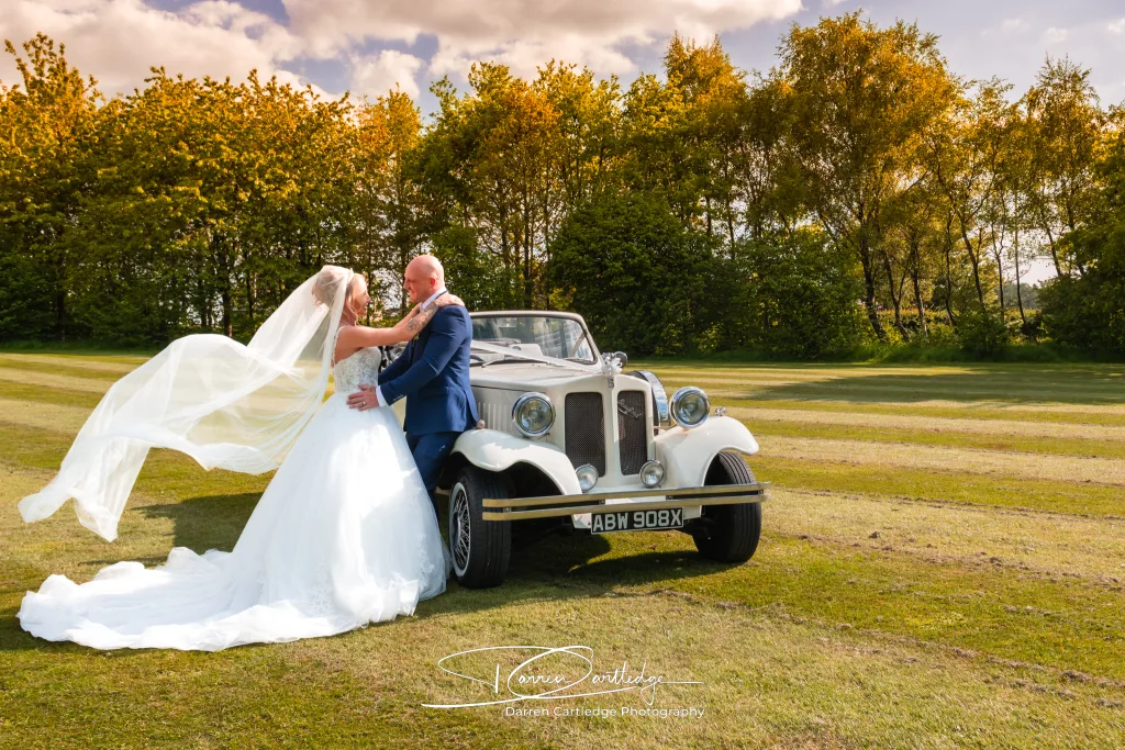 Bride and groom by their wedding car with the bride’s veil flowing during a Yorkshire wedding